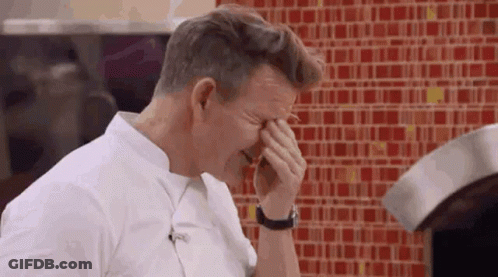A Man Is Covering His Face With His Hands In Front Of A Red Tiled Wall . GIF