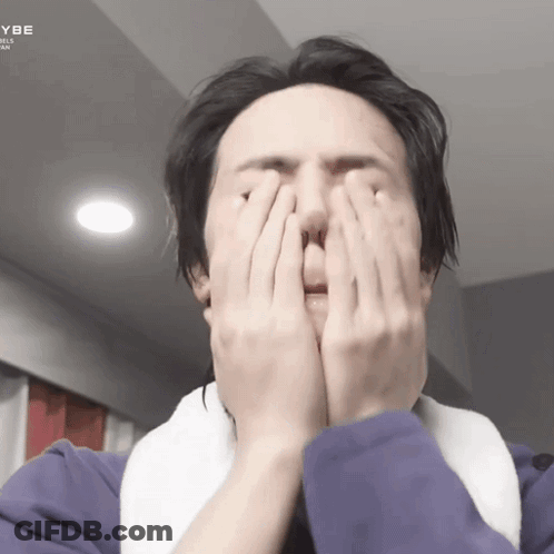 A Man Is Covering His Face With His Hands While Wearing A Purple Jacket GIF