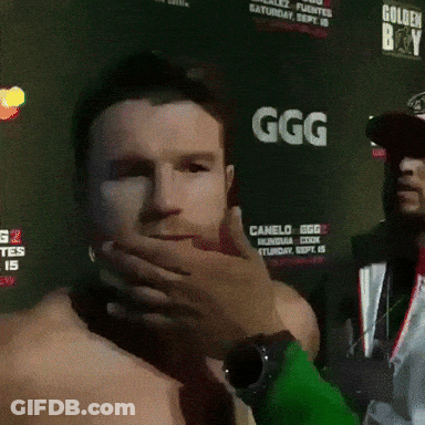 A Man Is Covering His Mouth In Front Of A Sign That Says Ggg GIF