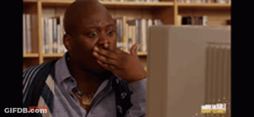 A Man Is Covering His Mouth With His Hand While Looking At A Computer Monitor . GIF