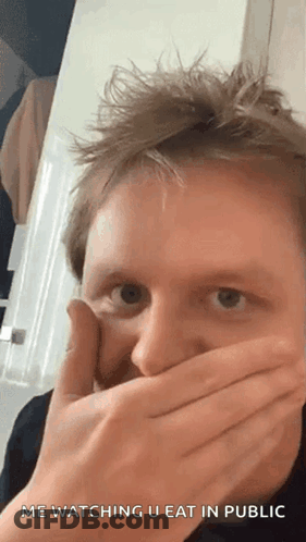A Man Is Covering His Mouth With His Hands While Looking At The Camera . GIF
