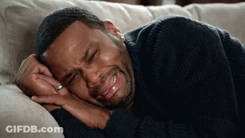 A Man Is Crying While Laying On A Couch With His Eyes Closed . GIF
