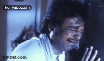 A Man Is Crying While Leaning Against A Wall With His Eyes Closed . GIF