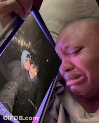 A Man Is Crying While Looking At A Picture Of Himself And Another Man On A Phone GIF