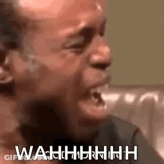 A Man Is Crying While Sitting On A Couch With His Mouth Open And The Words Wahh Written On His Face . GIF
