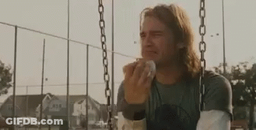 A Man Is Crying While Sitting On A Swing And Eating A Sandwich . GIF