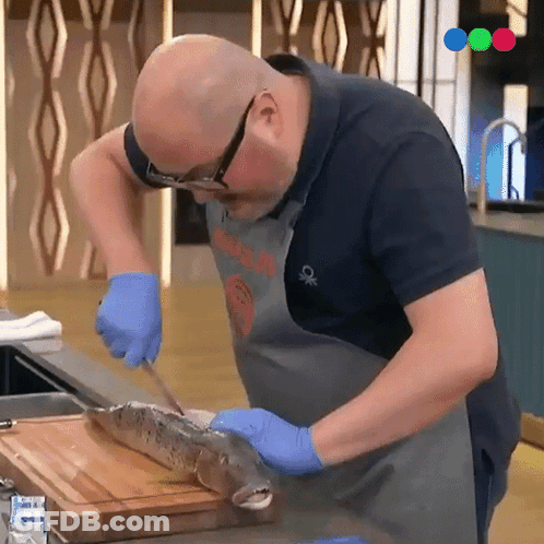 A Man Is Cutting A Fish On A Cutting Board While Wearing A Shirt That Says Benetton GIF