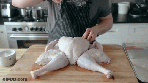 A Man Is Cutting A Turkey On A Wooden Cutting Board GIF