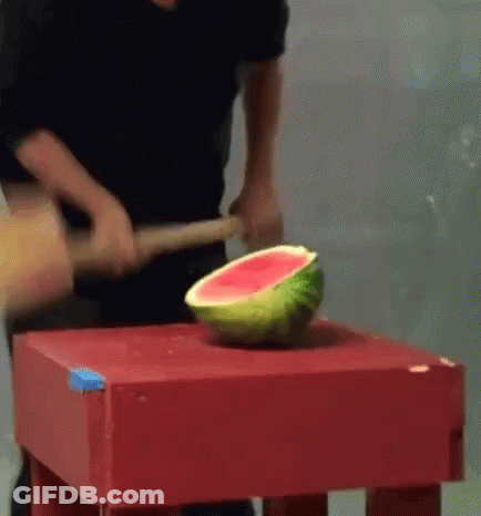 A Man Is Cutting A Watermelon With A Hammer On A Table . GIF