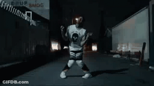 A Man Is Dancing In A Dark Alleyway At Night . GIF