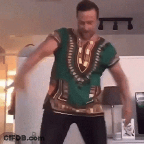 A Man Is Dancing In A Living Room Wearing A Green Shirt . GIF