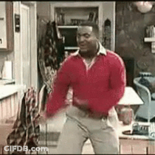 A Man Is Dancing In A Living Room Wearing A Red Sweater And Khaki Pants . GIF