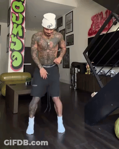 A Man Is Dancing In A Living Room With A Graffiti Wall That Says ' Dunzo ' On It GIF