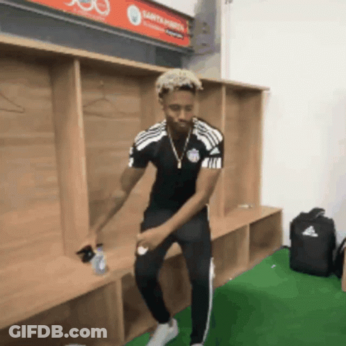 A Man Is Dancing In A Locker Room With A Sign That Says Santander On It GIF