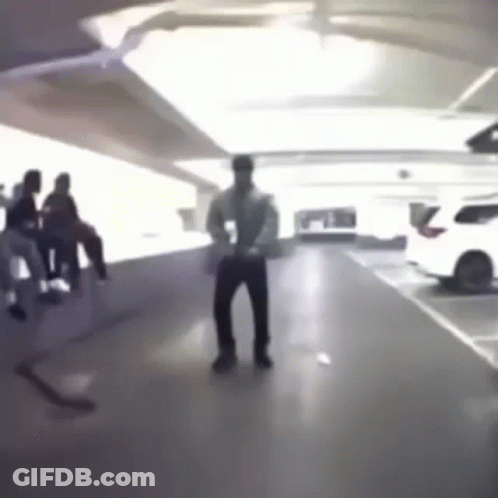 A Man Is Dancing In A Parking Garage While A Group Of People Sit On A Bench . GIF