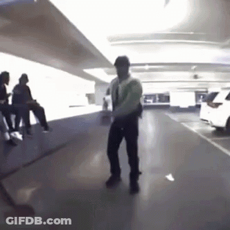A Man Is Dancing In A Parking Garage With People Sitting On Benches . GIF