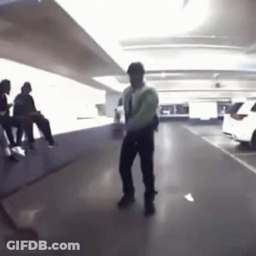 A Man Is Dancing In A Parking Garage With People Sitting On The Floor . GIF
