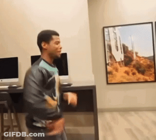 A Man Is Dancing In A Room With A Picture Of Hollywood On The Wall . GIF