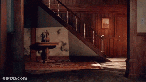 A Man Is Dancing In A Room With Stairs Behind Him GIF
