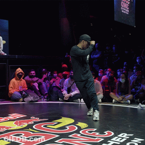 A Man Is Dancing In Front Of A Crowd That Is Sitting On The Floor Watching GIF