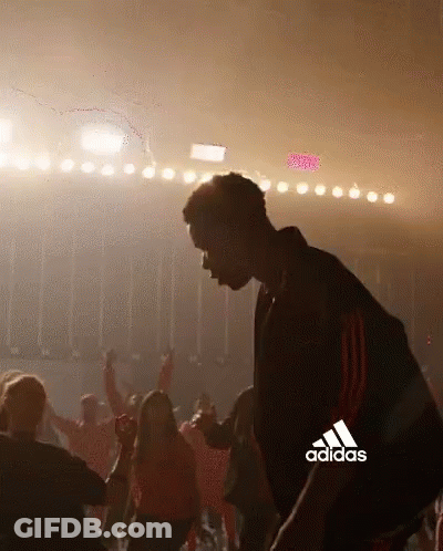 A Man Is Dancing In Front Of A Crowd With The Adidas Logo In The Background . GIF