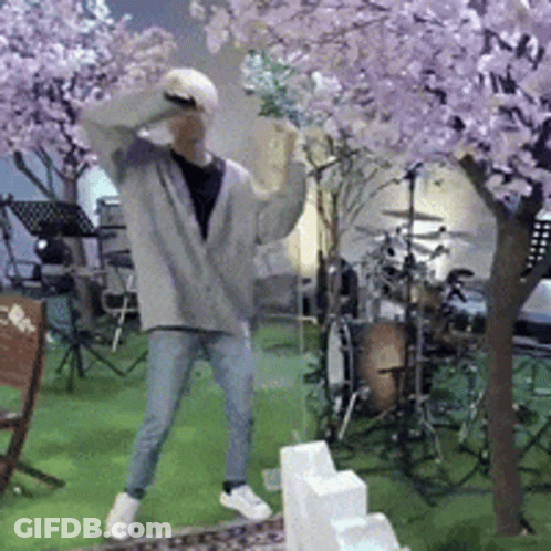 A Man Is Dancing In Front Of A Drum Set And A Cherry Blossom Tree GIF