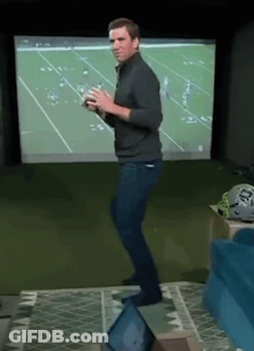 A Man Is Dancing In Front Of A Football Screen While Holding A Football . GIF