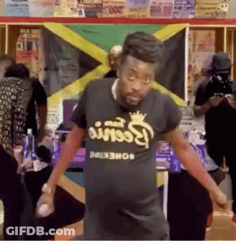 A Man Is Dancing In Front Of A Jamaican Flag In A Room . GIF