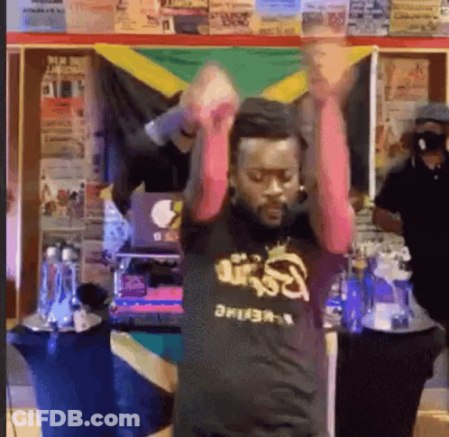 A Man Is Dancing In Front Of A Jamaican Flag While Wearing A Black Shirt . GIF
