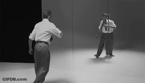 A Man Is Dancing In Front Of A Mirror GIF