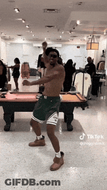 A Man Is Dancing In Front Of A Pool Table In A Store . GIF