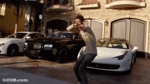 A Man Is Dancing In Front Of A Row Of Cars In A Driveway . GIF