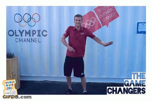 A Man Is Dancing In Front Of A Sign For The Olympic Channel GIF