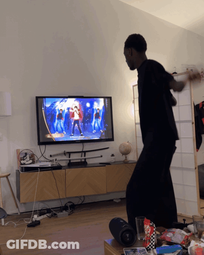 A Man Is Dancing In Front Of A Tv That Shows A Dance Video GIF