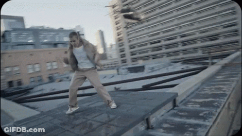 A Man Is Dancing On A Rooftop In Front Of A City Skyline GIF