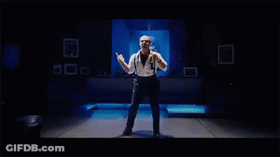 A Man Is Dancing On A Stage In A Dark Room . GIF