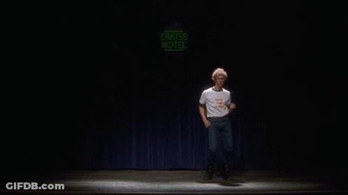 A Man Is Dancing On A Stage In Front Of A Neon Sign That Says Crates Motel GIF