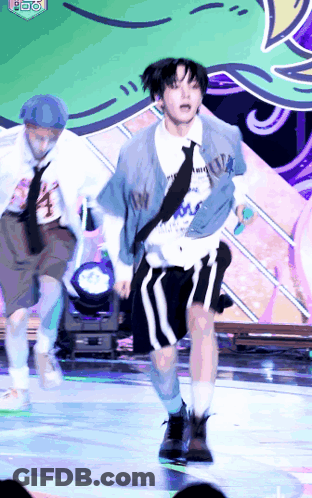 A Man Is Dancing On A Stage While Holding A Microphone And Wearing A Tie . GIF