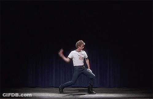 A Man Is Dancing On A Stage With A Blue Curtain Behind Him . GIF