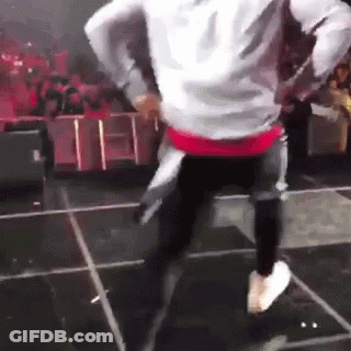 A Man Is Dancing On A Stage With A Crowd Watching . GIF