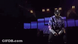 A Man Is Dancing On A Stage With A Knife In His Hand In A Dark Room . GIF