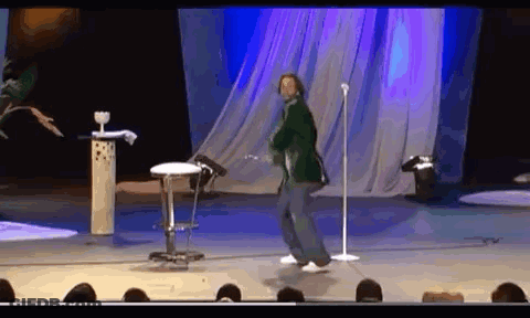 A Man Is Dancing On Stage In Front Of A Microphone . GIF