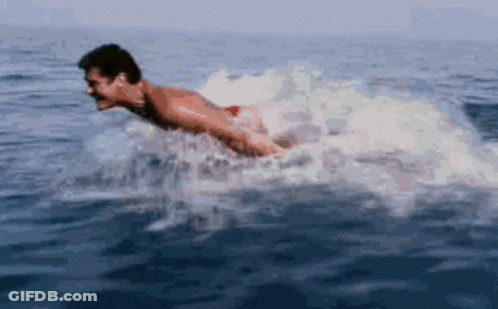 A Man Is Diving Into The Ocean With A Shark Behind Him GIF
