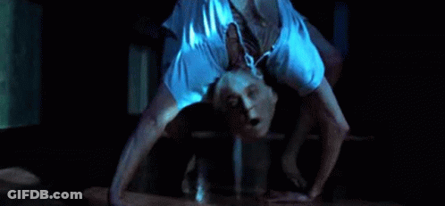 A Man Is Doing A Handstand On The Floor In A Dark Room With His Mouth Open . GIF