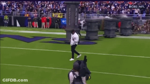 A Man Is Doing A Trick On A Football Field In Front Of A Ravens Sign GIF