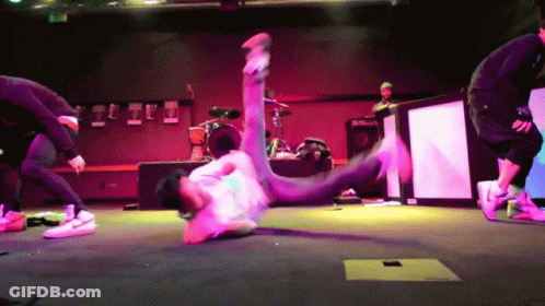 A Man Is Doing A Trick On A Stage With A Drum Set In The Background GIF