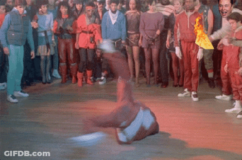 A Man Is Doing A Trick On The Floor In Front Of A Crowd Of People GIF