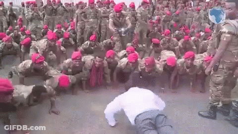 A Man Is Doing Push Ups In Front Of A Large Group Of Soldiers Wearing Red Hats . GIF
