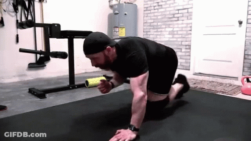 A Man Is Doing Push Ups On A Mat In A Gym While Holding A Roller . GIF