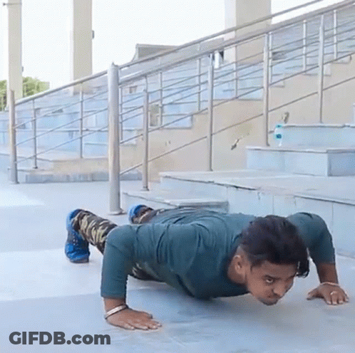 A Man Is Doing Push Ups On A Sidewalk In Front Of Some Stairs GIF